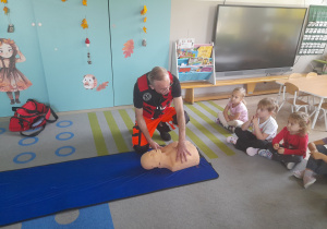 Pan ratownik demonstruje dzieciom na fantomie jak ratować człowieka.