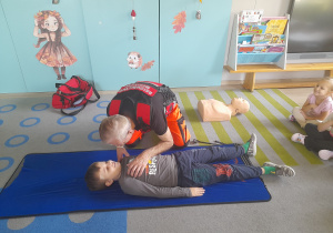 Pan ratownik demonstruje na dziecku jak sprawdzić czy osoba jest przytomna.