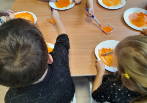 Dzieci malują farbą talerzyki papierowe.