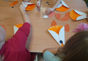 Dzieci przyklejają elementy do swoich lisków.