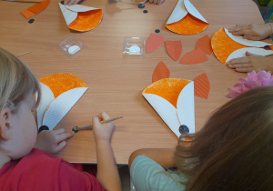 Dzieci przyklejają elementy do swoich lisków.