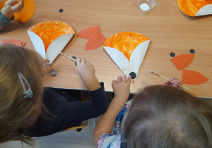 Dzieci przyklejają elementy do swoich lisków.