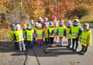 Dzieci pozują do zdjęcia w parku, na tle drzew w kolorach jesieni.