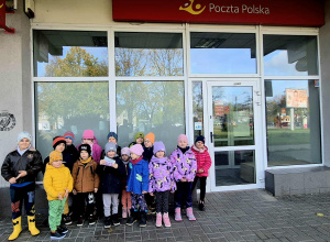 Dzieci pozują do zdjęcia przed budynkiem poczty