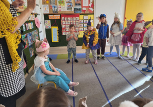 Dziewczynka przebrana za królewnę siedzi na krześle, pozostałe dzieci stoją,