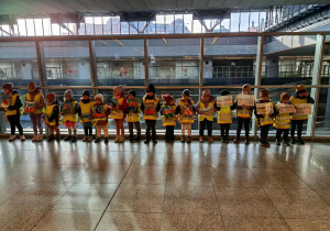 Dzieci ustawione w szeregu, trzymają ilustracje.