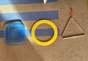 Figury geometryczne ułozone z pokrywki po pudełku, instrumentu muzycznego i przyboru do ćwiczeń.