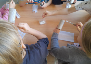 Dzieci smarują rolkę klejem.