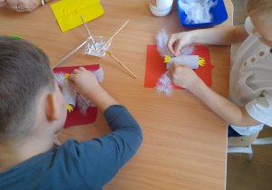 Dzieci przyklejają elementy do swoich prac.