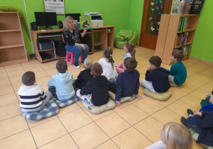 Dzieci słuchają książki czytanej przez Panią bibliotekarkę.