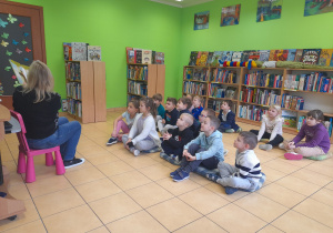 Dzieci słuchają książki czytanej przez Panią bibliotekarkę.