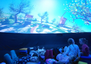 Dzieci leżą w środku kopuły planetarium, oglądają wyświetlaną animację.