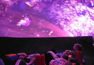 Dzieci leżą w środku kopuły planetarium, oglądają wyświetlaną animację.