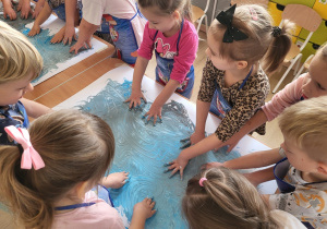 Dzieci dłońmi rozprowadzają farbę po kartonach do muzyki.