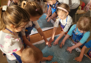 Dzieci dłońmi rozprowadzają farbę po kartonach do muzyki.