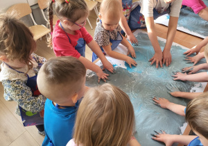 Dzieci dłońmi rozprowadzają farbę po kartonach do muzyki.