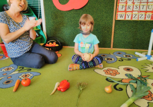 Dziecko rozpoznaje warzywo po dotyku, pod kierunkiem nauczycielki.