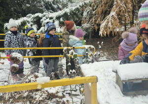 Dzieci wsypują ziarenka do karmnika.