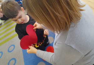 Chłopiec przebija papierowe srece pinezką.