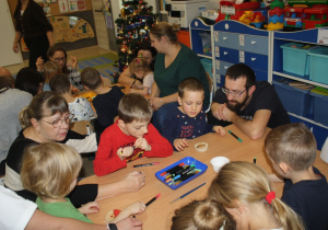 Dzieci z rodzicami ozdabiają plastry drzewa.