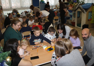 Dzieci z rodzicami ozdabiają plastry drzewa.