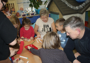 Dzieci z rodzicami ozdabiają plastry drzewa.