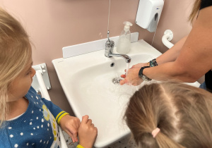 Nauczycielka prezentuje schemat mycia rak.