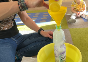 Nauczycielka wlewa wodę do buteli wypchanej papierem toaletowym.