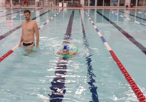 Dziecko pływa w basenie pod kierunkiem instruktora