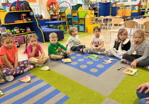 Dzieci siedzą na dywanie z ilustracja kredki.