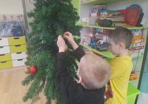 Chłopcy ubierają choinkę.