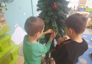 Chłopcy ubierają choinkę.