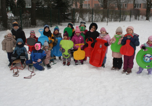 Dzieci stoją na śniegu w oczekiwaniu na zjazd z górki.