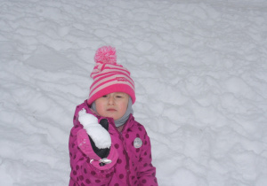 Dziewczynka trzyma kulkę ze śniegu w rączce.