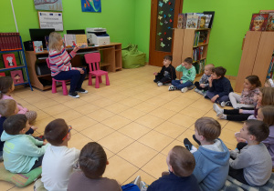 Dzieci słuchają bajki czytanej przez Panią pracującą w bibliotece.