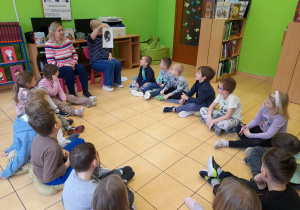 Dzieci siedzą w kole i oglądają ilustracje.