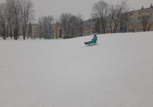 Dziecko zjeżdża z górki na sankach.