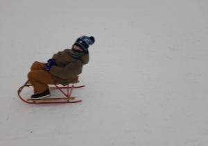 Dziecko zjeżdża z górki na sankach.