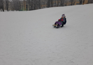 Dzieci zjeżdżają na sankach z górki.