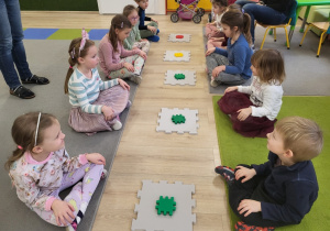 Dzieci siedzą w dwóch rzędach, przed nimi leżą puzlle.