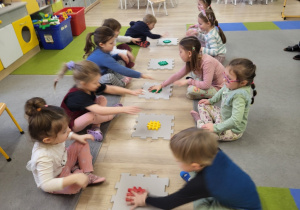 Dzieci siedzą w dwóch rzędach, przed nimi leżą puzlle.