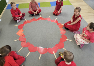 Dzieci siedzą w kole, serduszka leżą na dywanie w kole.