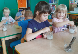 Dzieci mieszają łyżeczką desery.