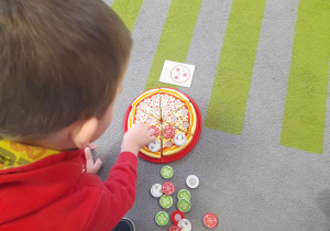 Chłopiec układa na pizzy składniki.