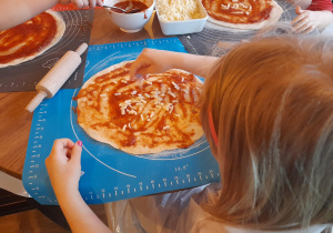 Dziewczynka sypie ser na pizzę.