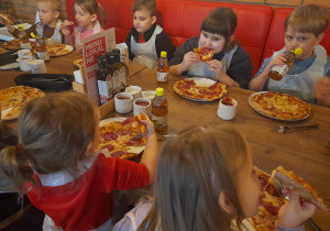 Dzieci zjadają przygotowane samodzielnie pizze.