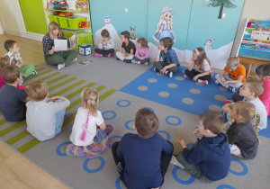 Dzieci słuchają opowiadania czytanego przez nauczycielkę.
