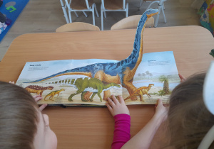 Dzieci oglądają książkę o dinozaurach.