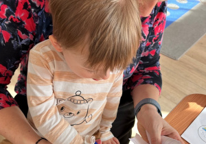 Chłopiec z pomocą nauczycielki wycina obrazki.