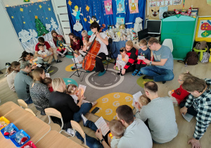 Dzieci siedzą w kole z rodzicami.